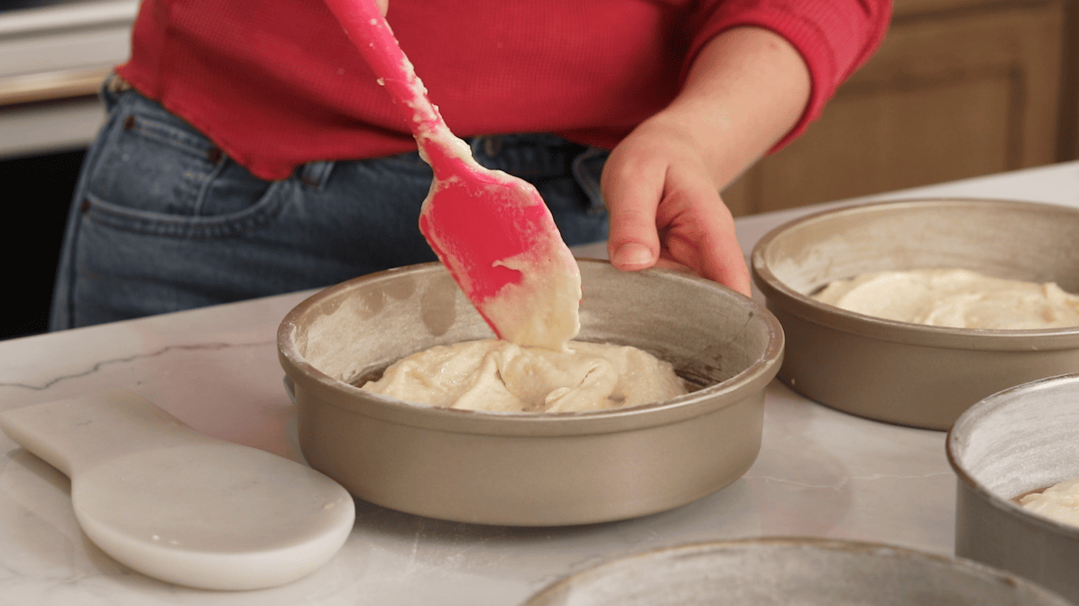 Spatula spreading cake batter into a round cake pan.