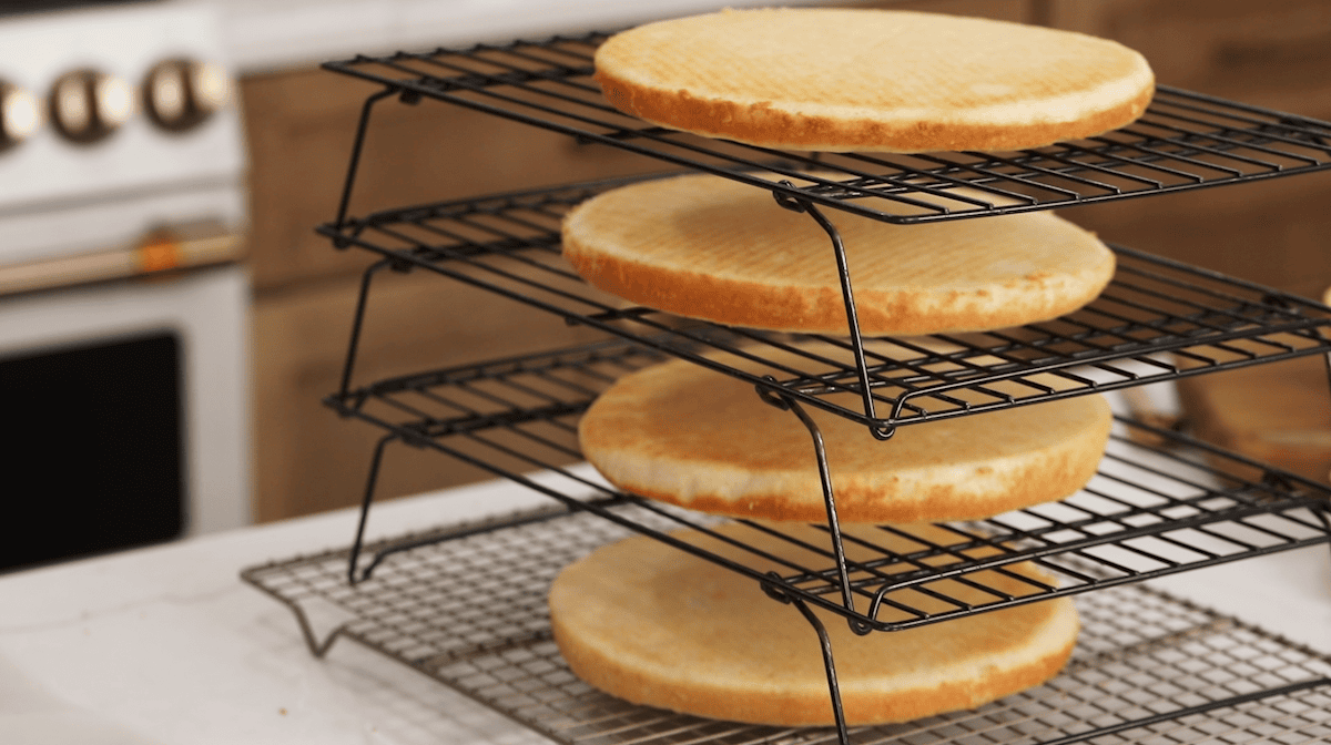 Four layers of cake cooling on cooling racks.