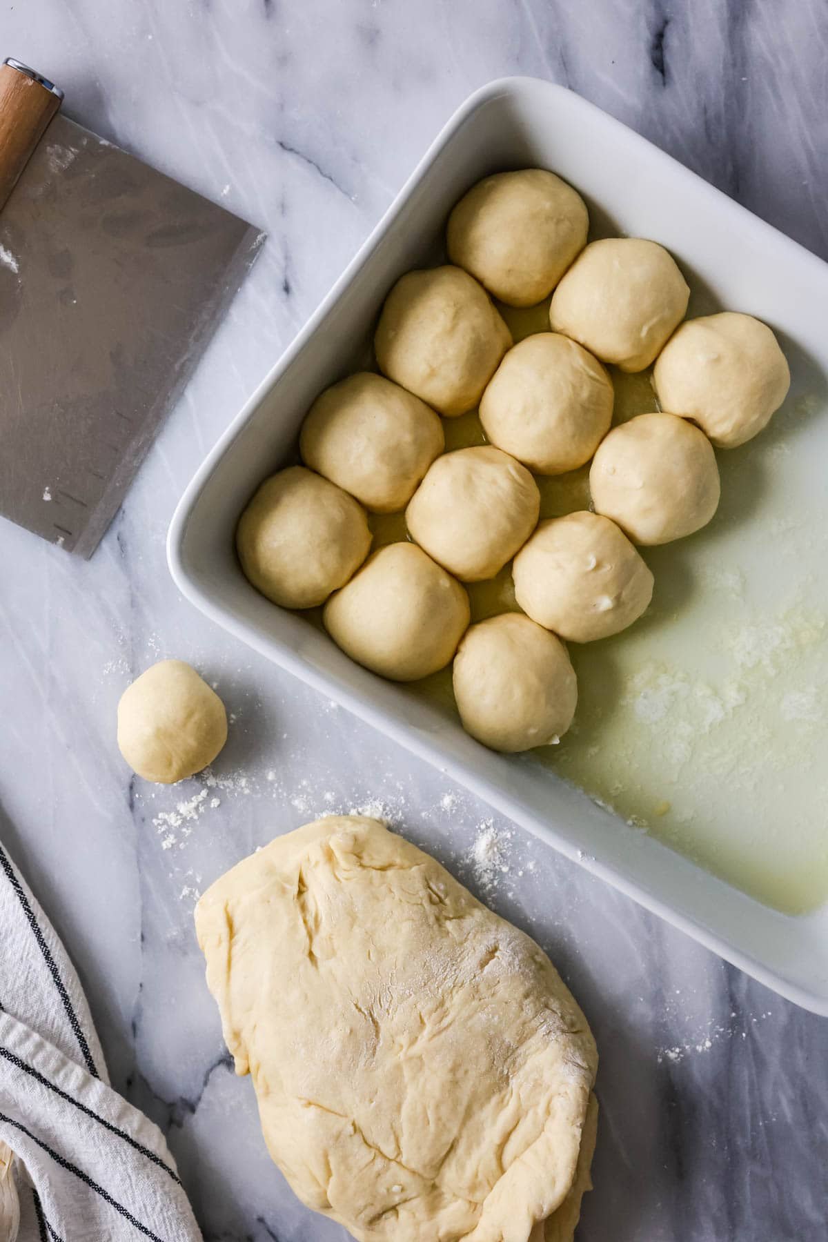 Dough being divided into balls and placed in a greased baking dish.