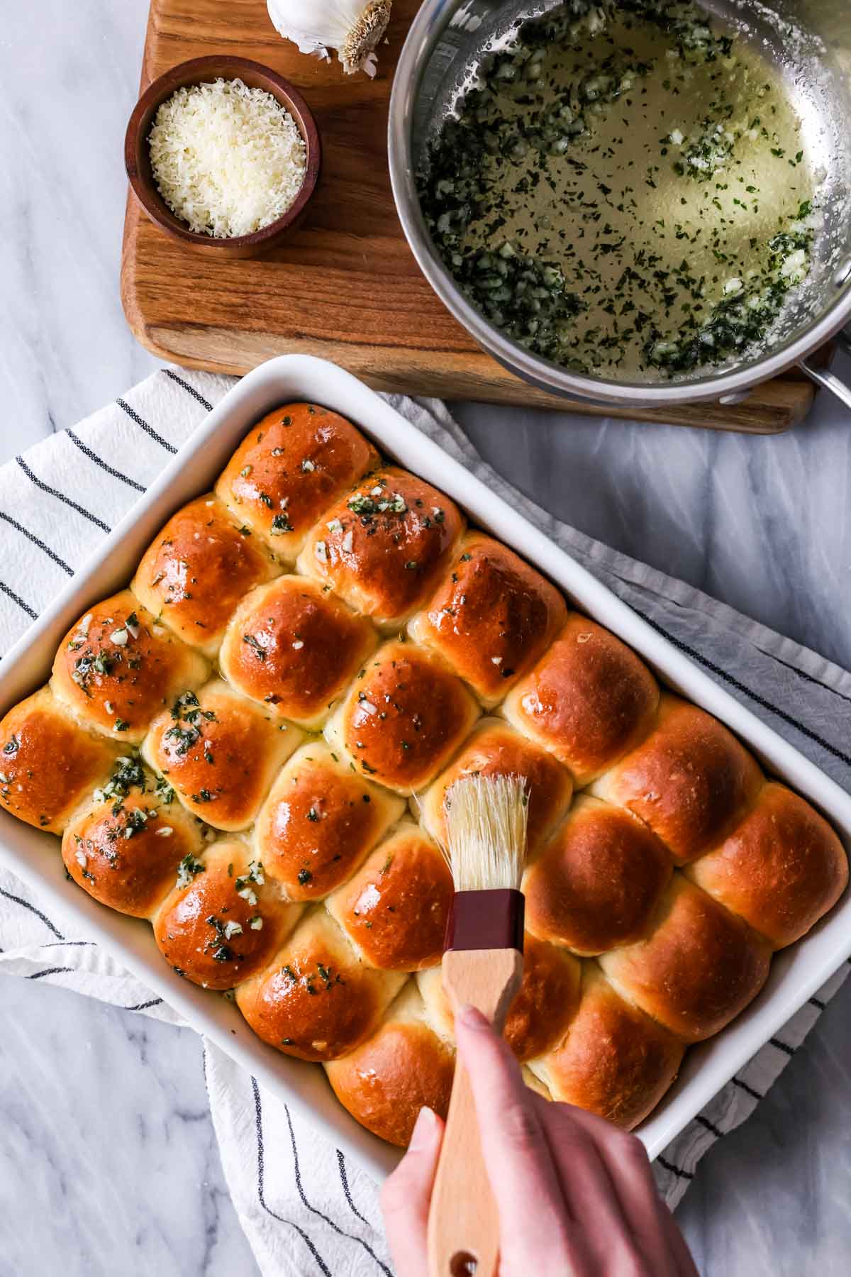 Brushing garlic butter over dinner rolls after baking.