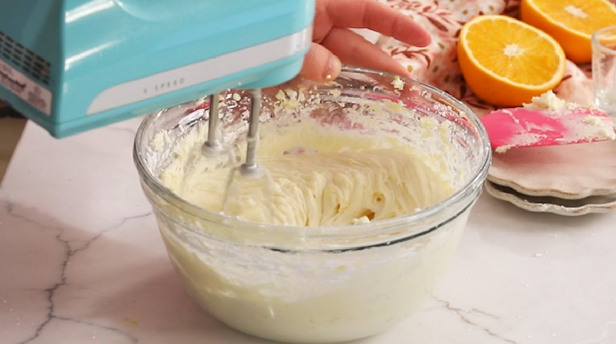 Hand mixer mixing frosting together in a bowl.