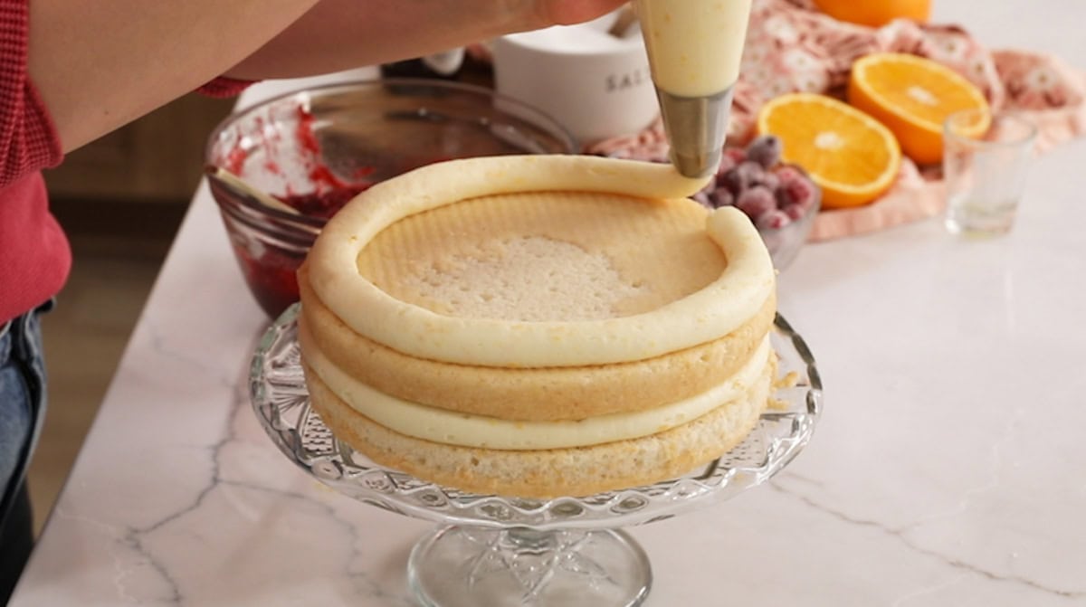 Piping a frosting dam onto the second layer of a cake.