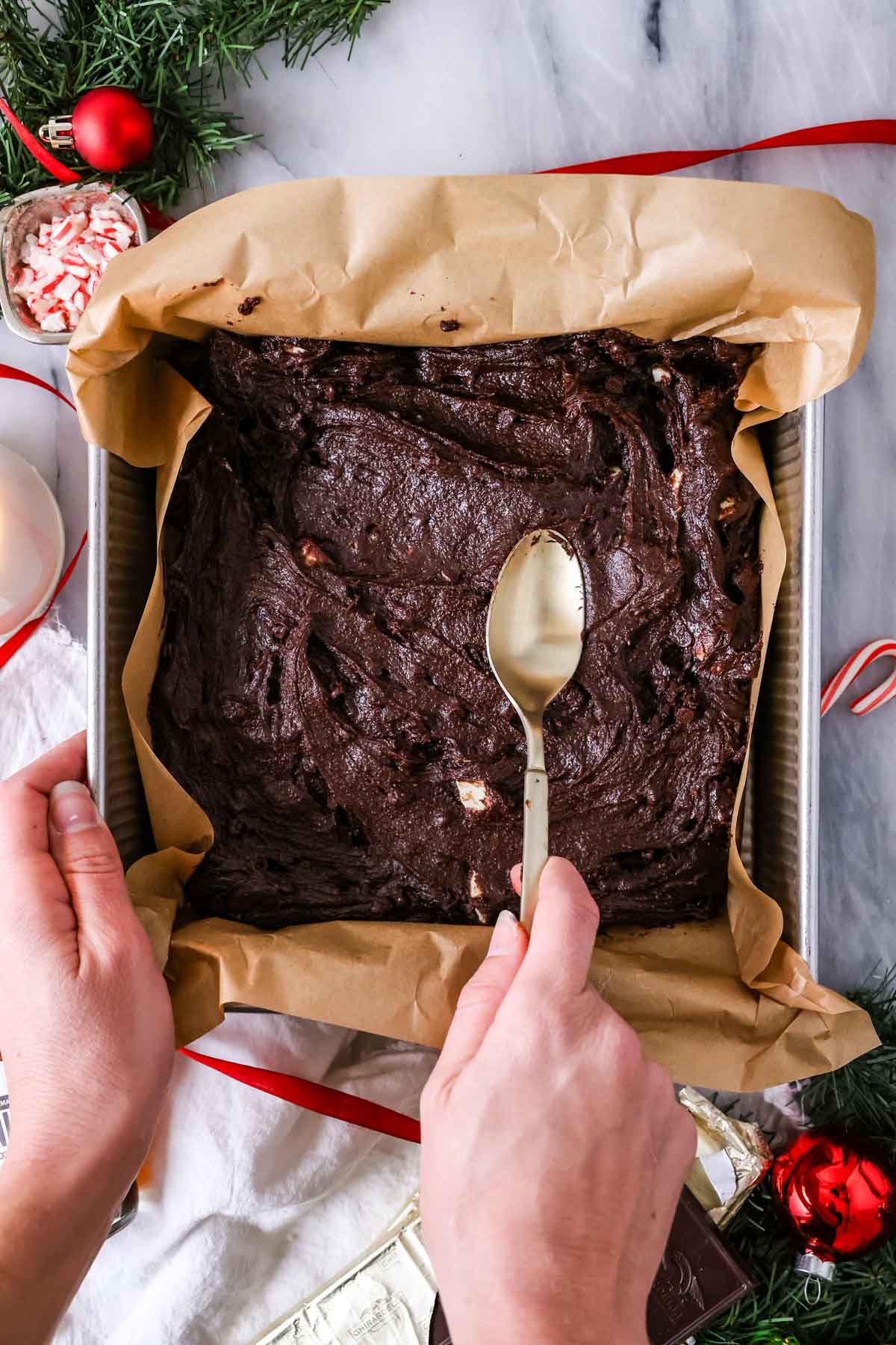 Spoon spreading brownie batter into a parchment lined pan.