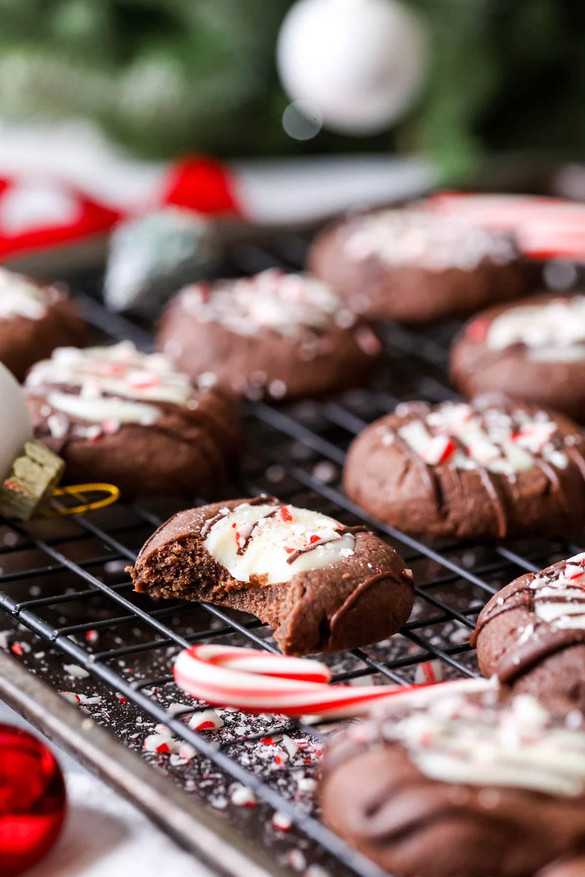 Bite missing from a chocolate peppermint thumbprint cookie on a cooling rack with more cookies.