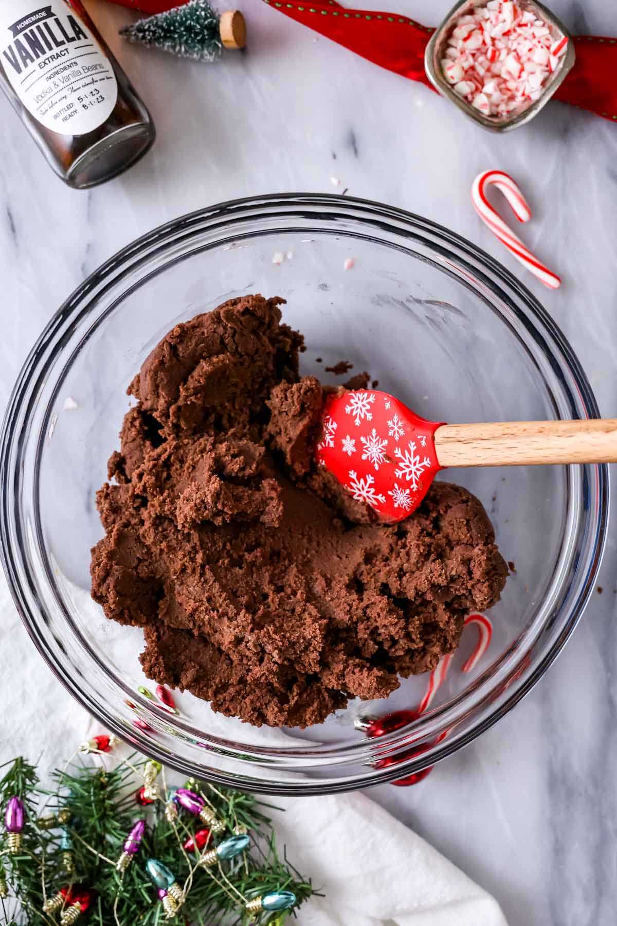 Overhead view of a bowl of chocolate cookie dough with a red snowflake spatula resting on top.