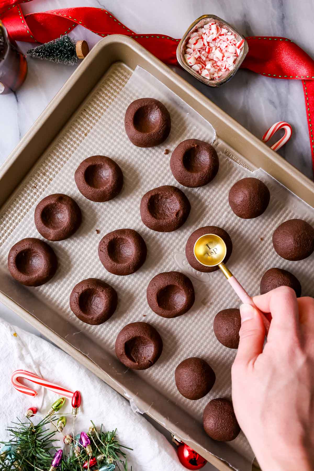 Using a teaspoon to make an indent in the center of chocolate cookies before baking.