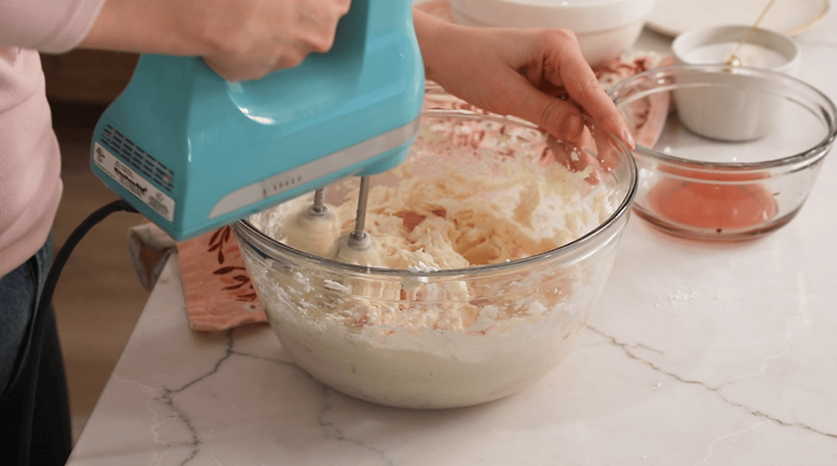 Incorporating pink champagne into buttercream with a mixer.