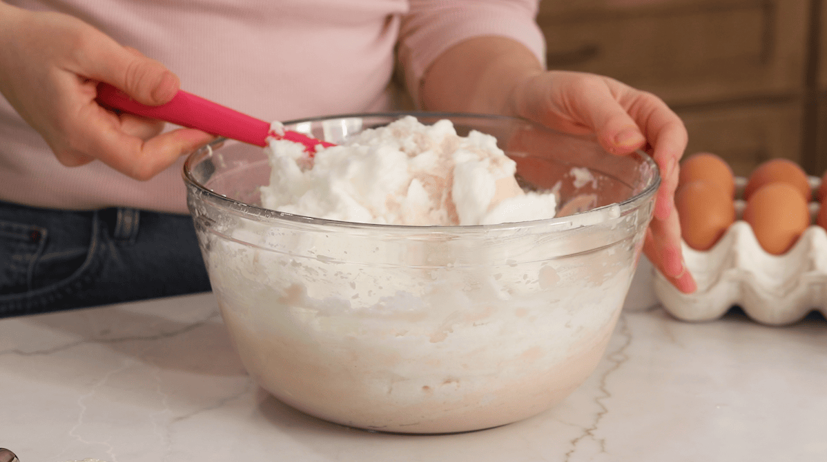 Folding egg whites into a pink cake batter.