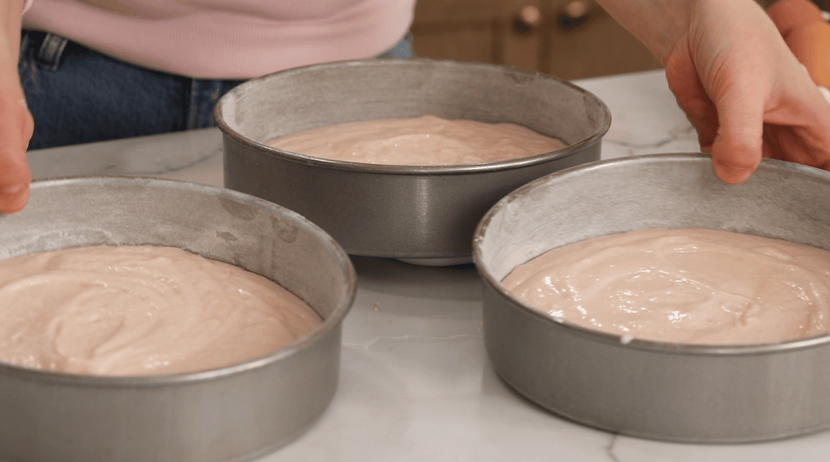 Three cake tins filled with pink cake batter before going in the oven.