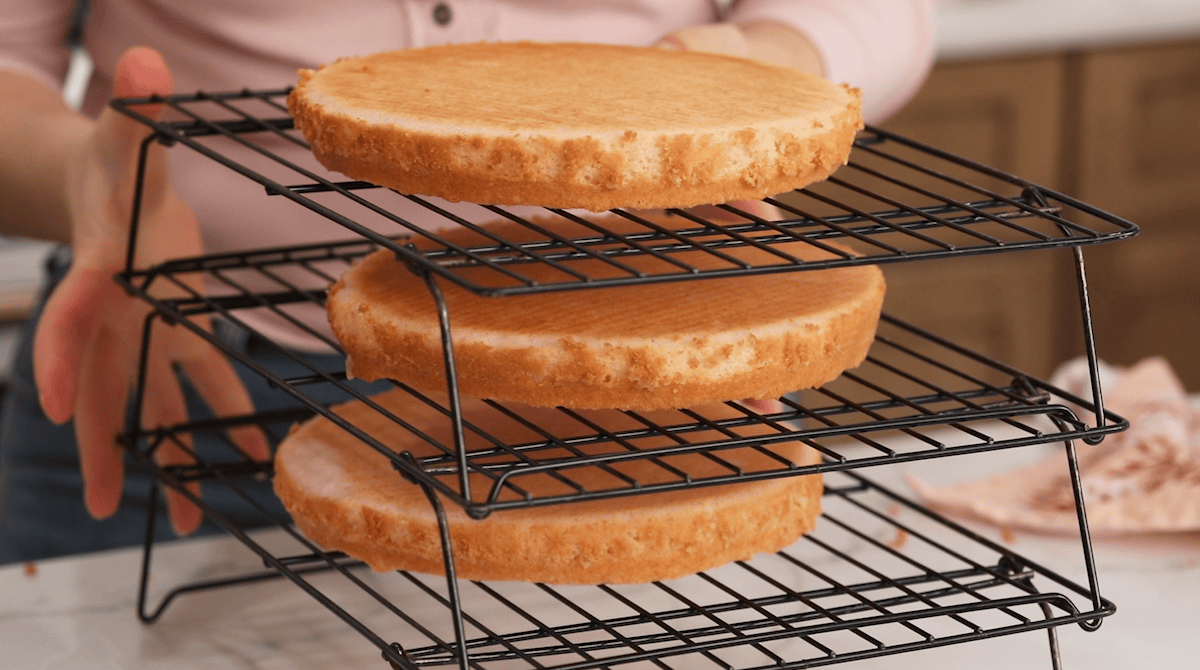 Three cake layers cooling on stacked cooling rack.