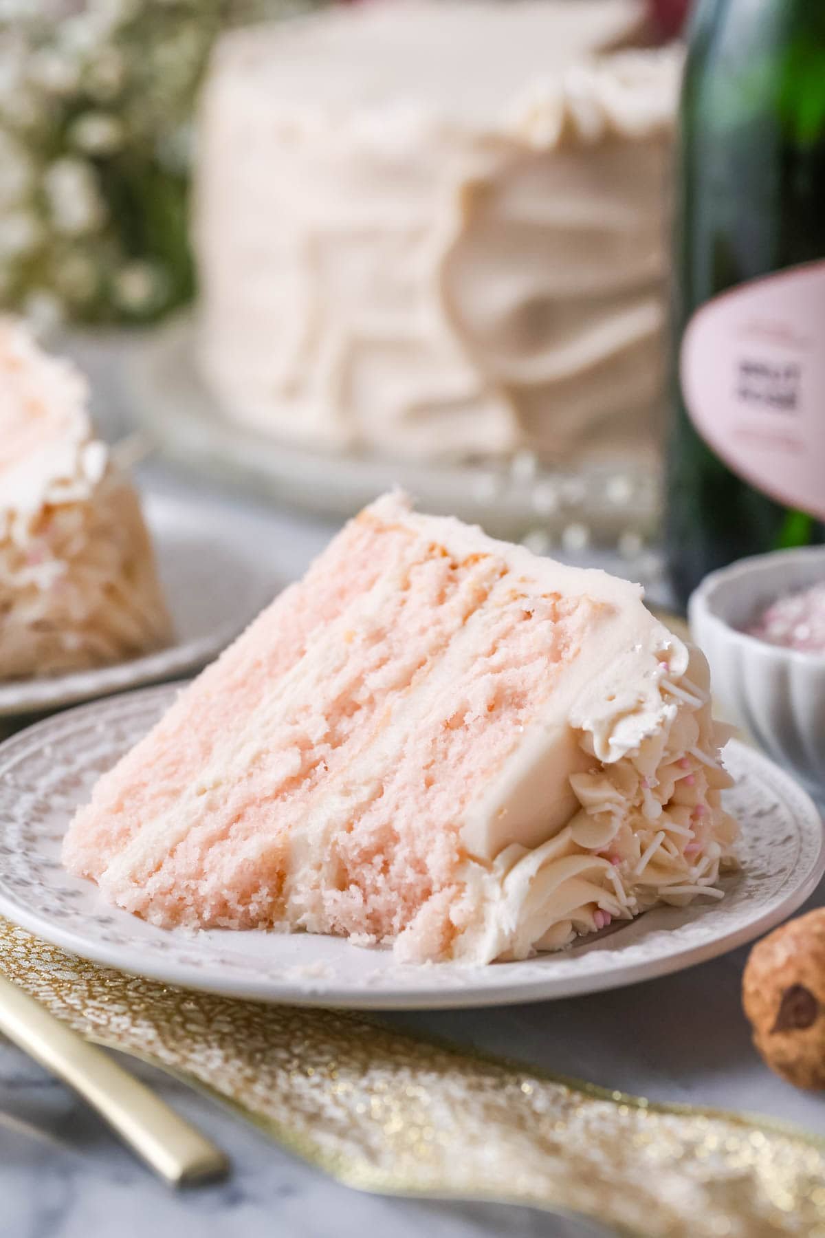 Slice of pink champagne cake on a plate with one bite missing.