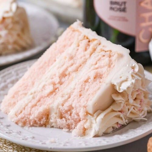 Slice of pink champagne cake on a plate with one bite missing.