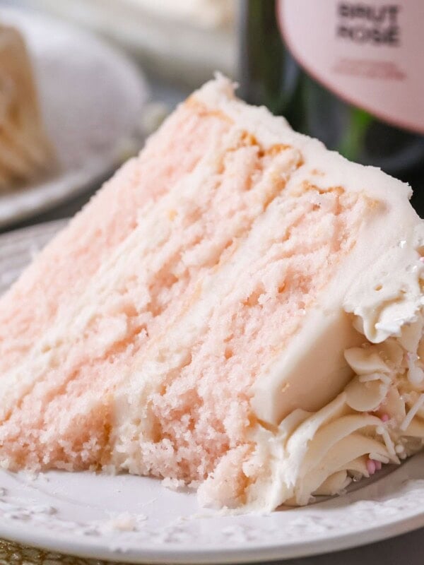 Slice of pink champagne cake on a plate with one bite missing.
