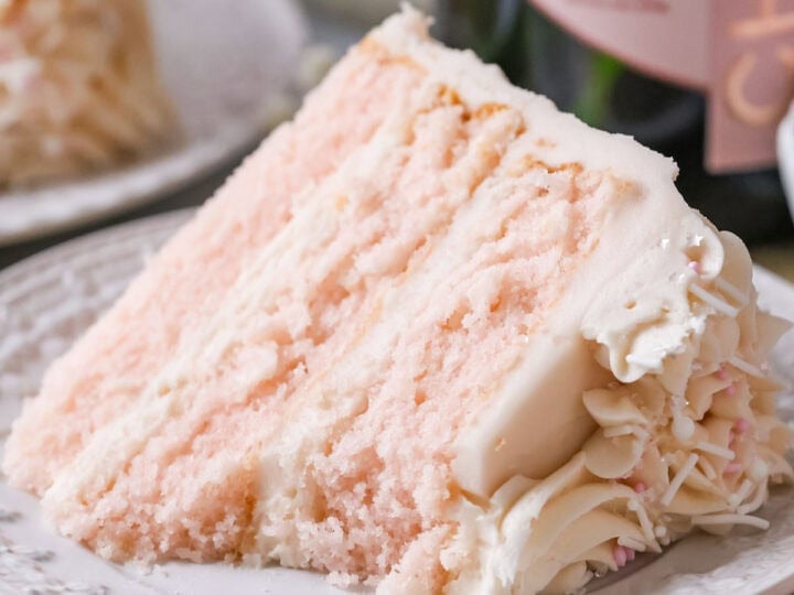 Slice of pink champagne cake on a plate with one bite missing.