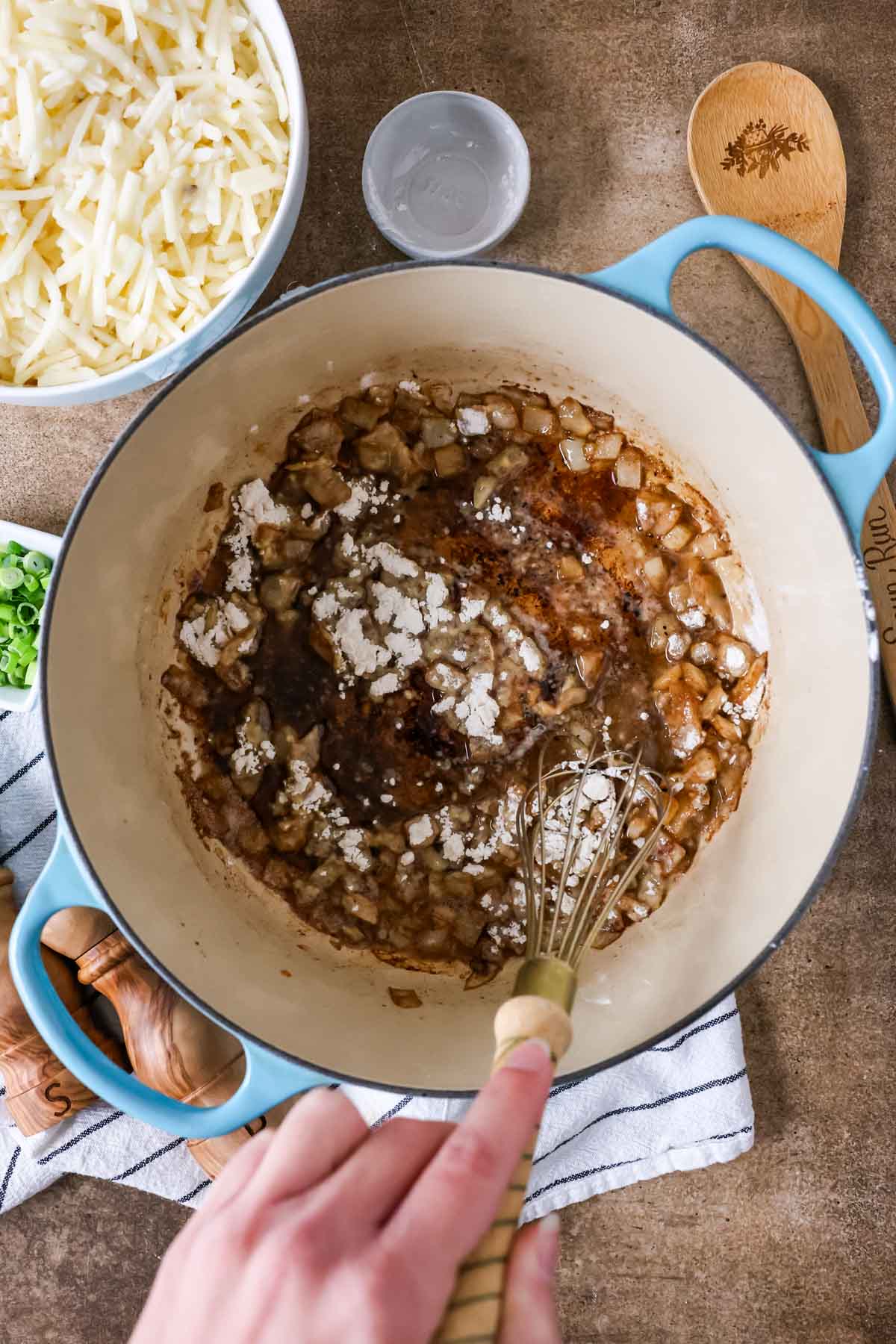 Overhead view of flour being stirred into diced onion cooking in a pot.