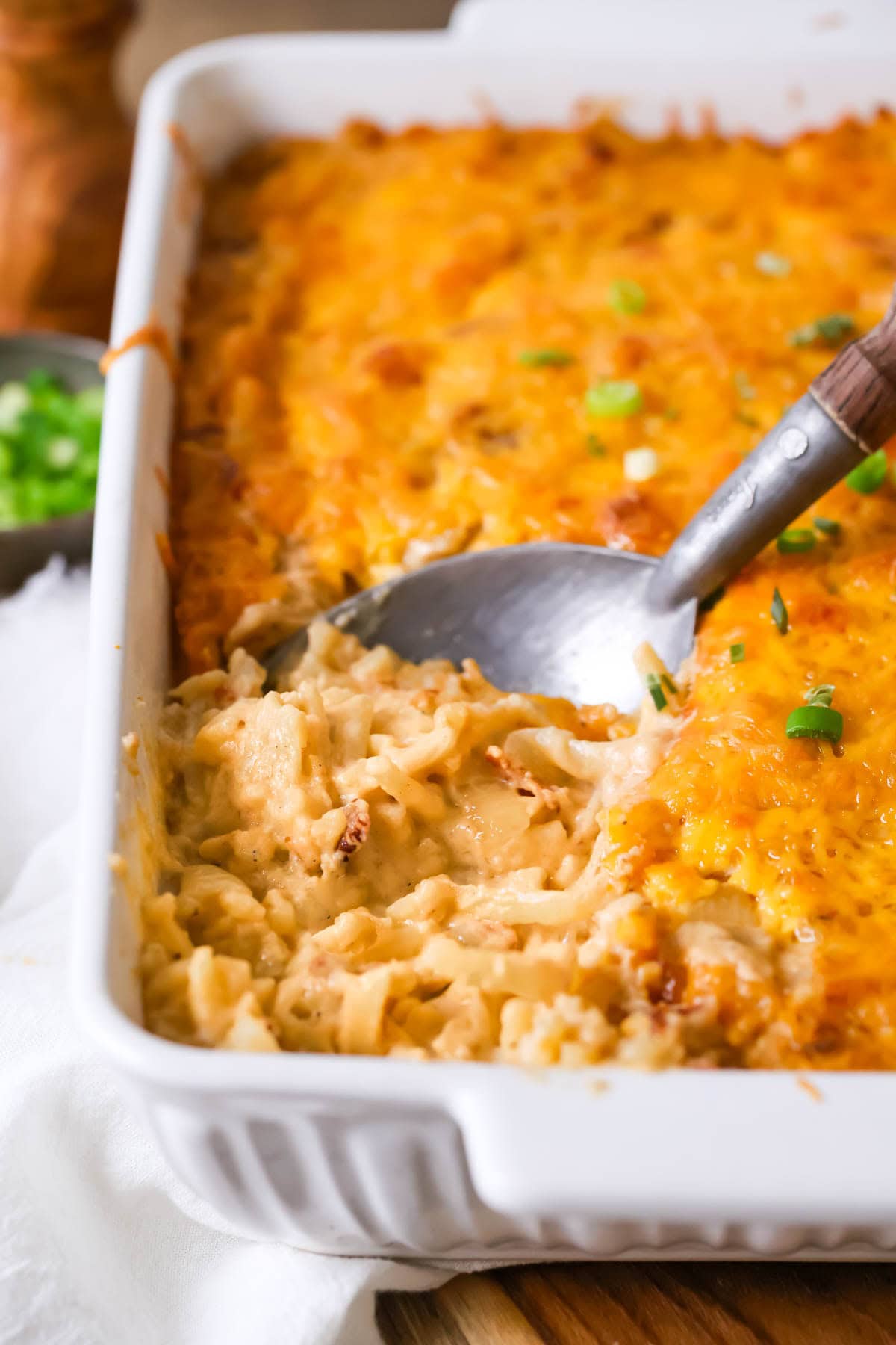 Spoon scooping a serving of hashbrown casserole out of a dish.