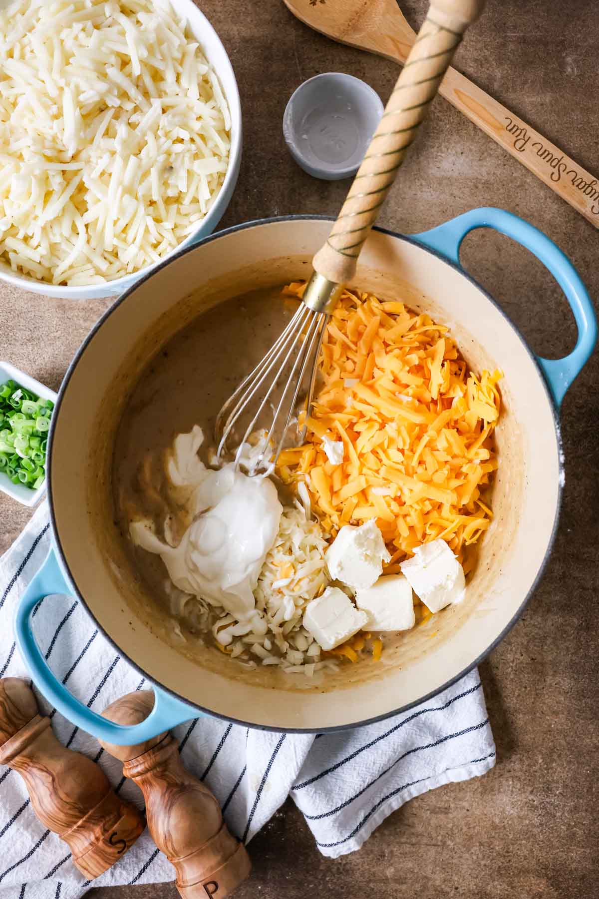 Overhead view of shredded cheese, cream cheese, and sour cream being stirred into a roux.