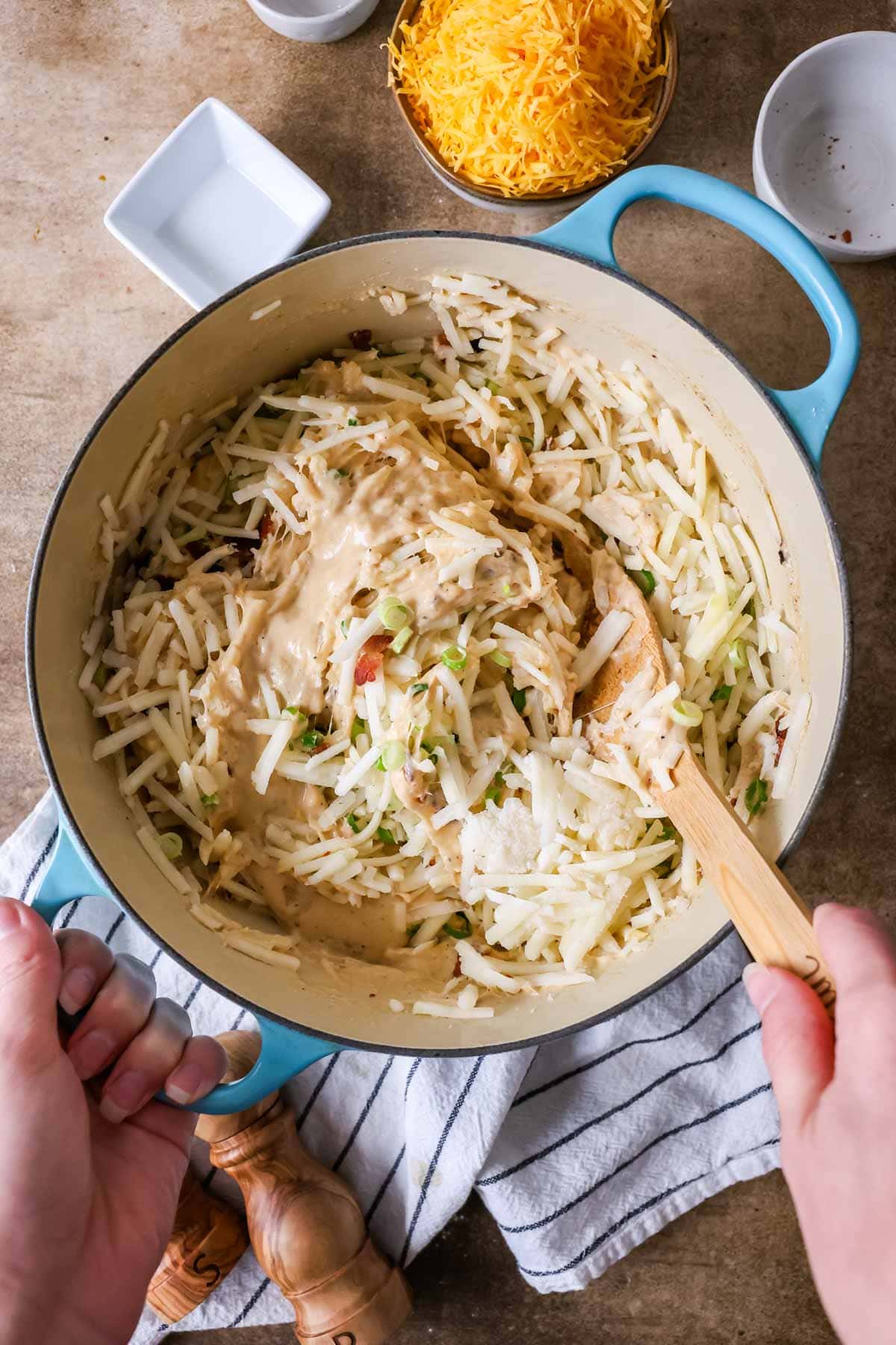 Overhead view of hash brown potatoes, bacon, and green onion being stirred into a cheese sauce.