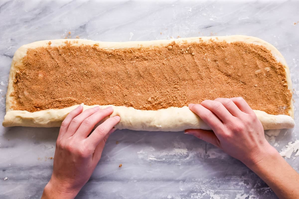 Overhead of hands rolling up cinnamon dough into a log.