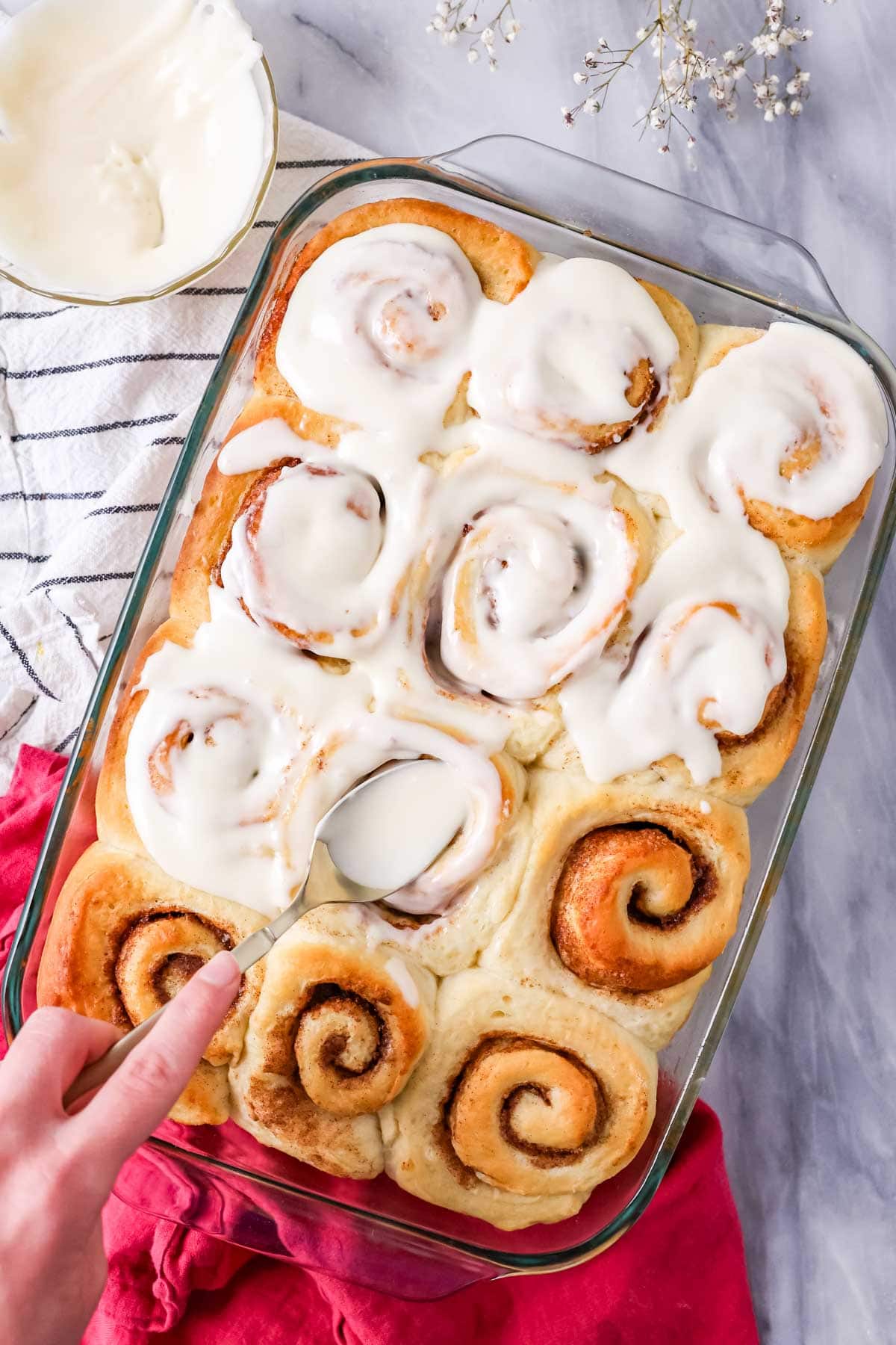 Overhead view of spreading cream cheese cinnamon roll icing on to Amish cinnamon rolls.
