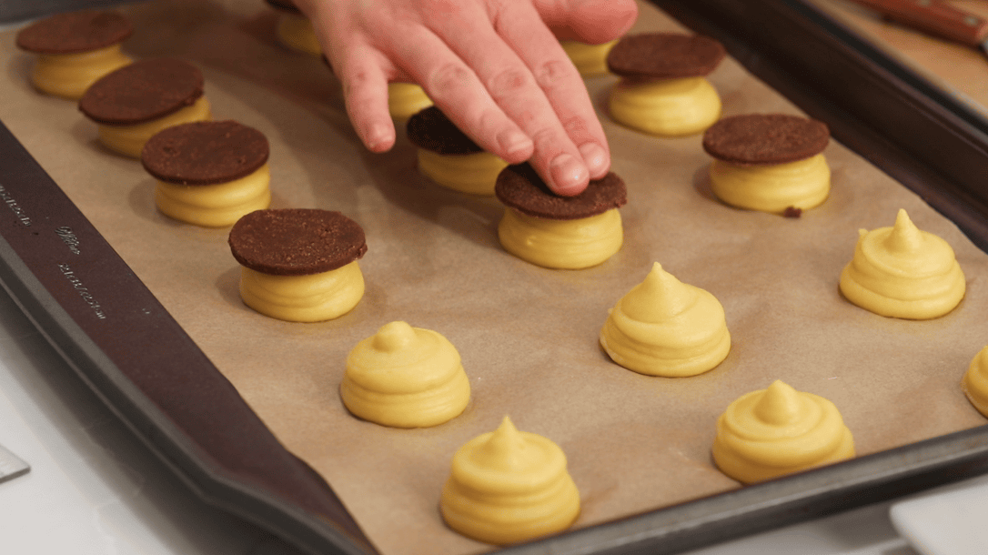 Pressing chocolate craquelin onto choux mounds before baking.