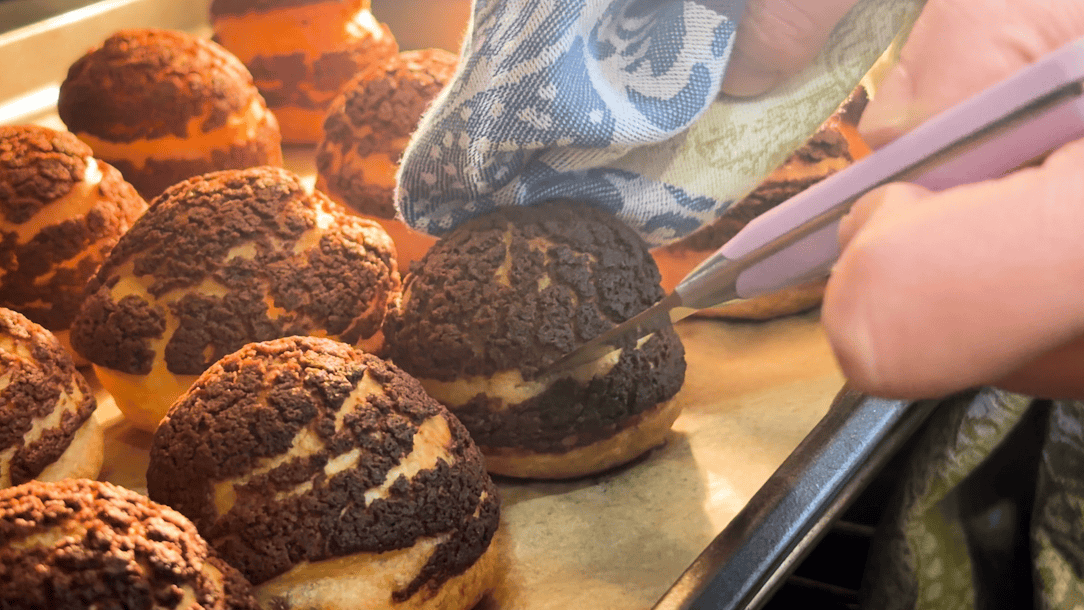 Piercing chocolate choux au craquelin with a knife to let the steam escape.