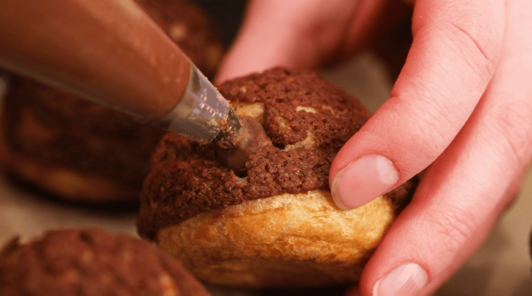Piping chocolate pastry cream into chocolate choux au craquelin.