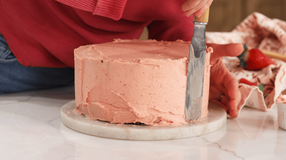 Cake being frosted with a strawberry frosting.