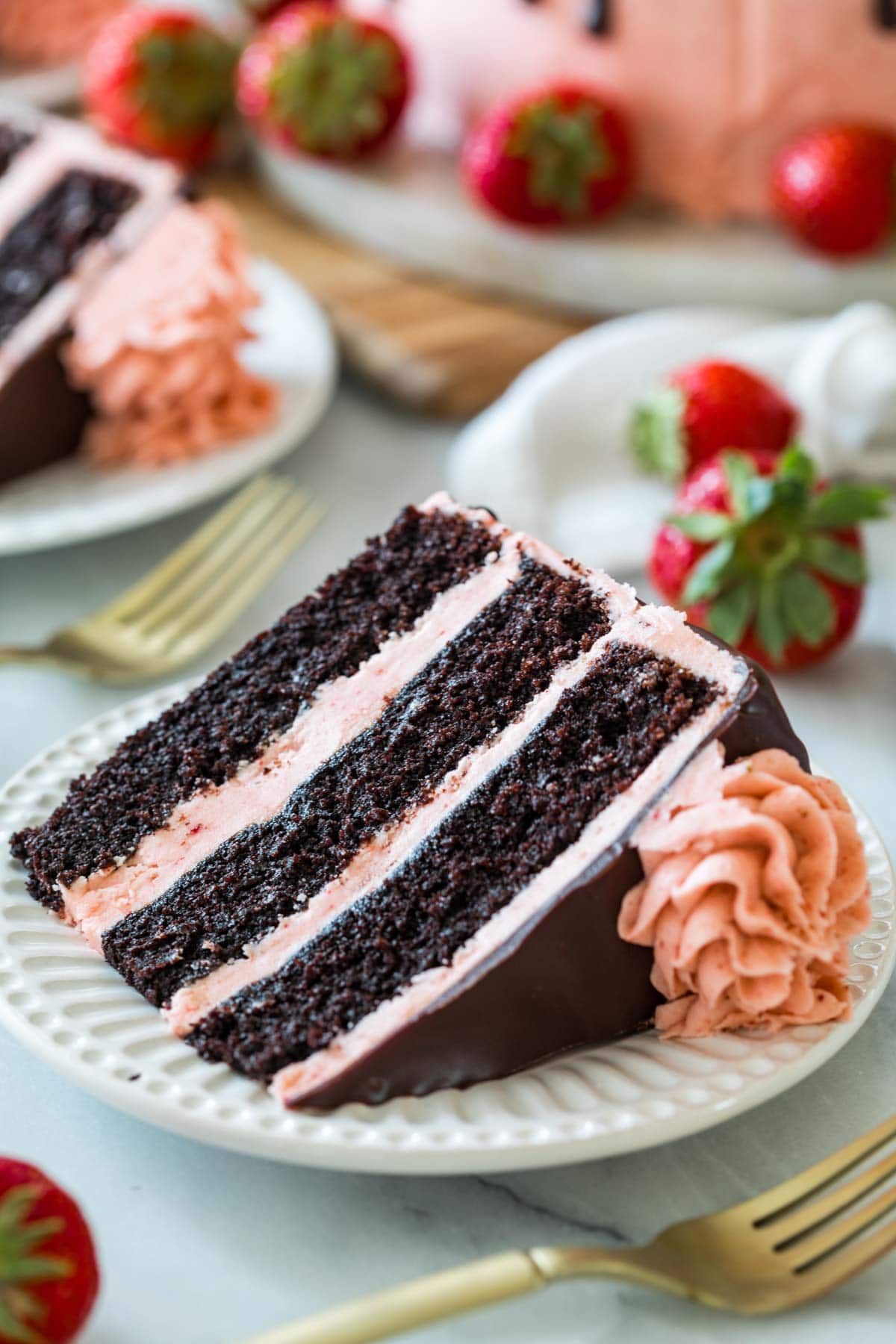 Slice of chocolate strawberry cake made with three layers of dark chocolate cake, strawberry frosting, and chocolate ganache.