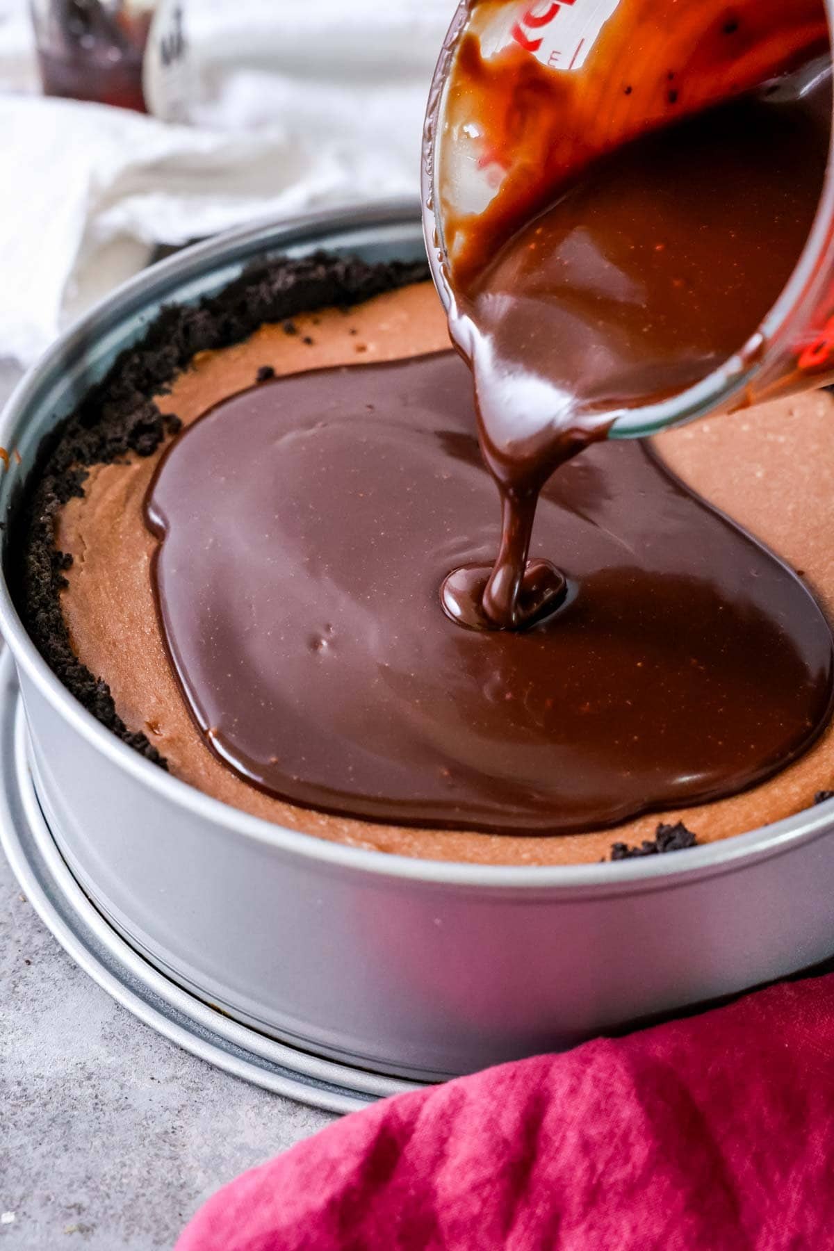 Nutella ganache being poured over a cheesecake in a springform pan.