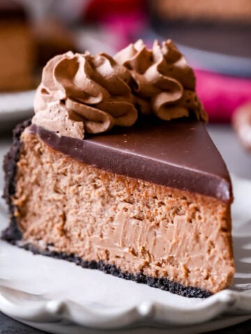 Slice of Nutella cheesecake topped with chocolate ganache and chocolate whipped cream. on a plate.