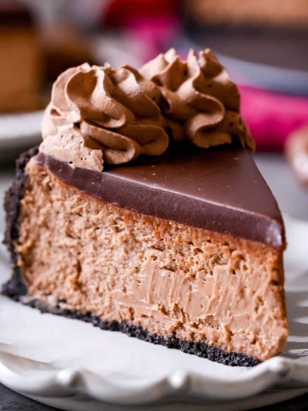 Slice of Nutella cheesecake topped with chocolate ganache and chocolate whipped cream. on a plate.
