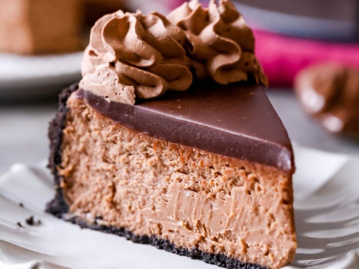 Slice of Nutella cheesecake topped with chocolate ganache and chocolate whipped cream. on a plate.