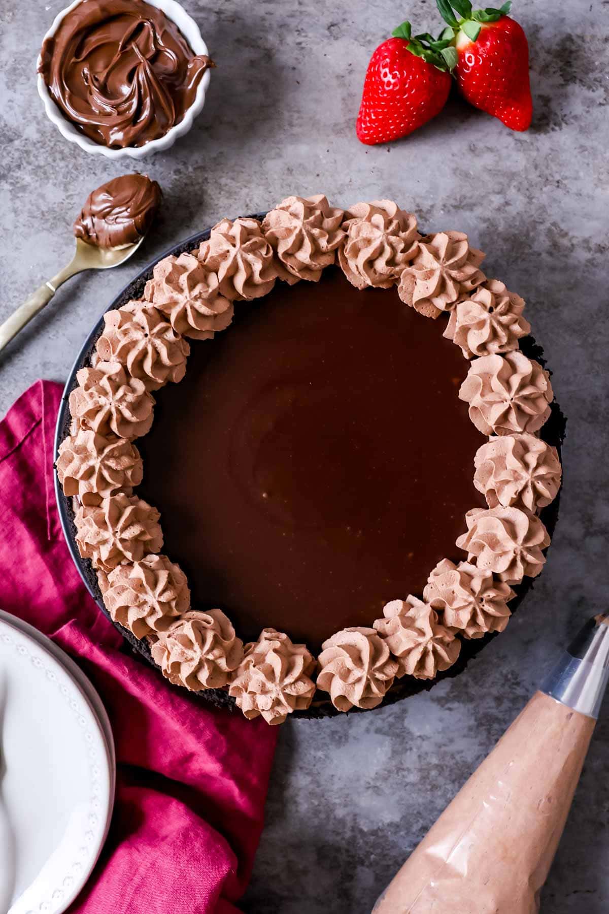 Overhead view of a cheesecake that's been topped with a Nutella ganache and piped dollops of chocolate whipped cream.