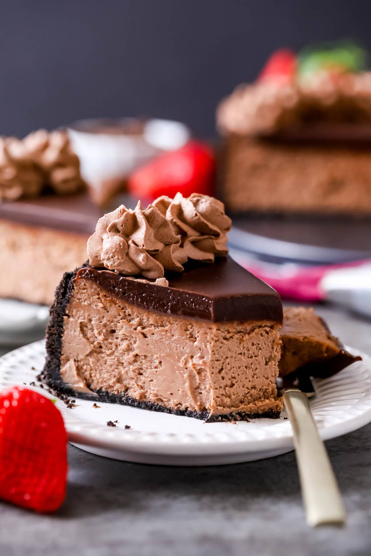 Bite missing from a slice of Nutella cheesecake topped with ganache and chocolate whipped cream.