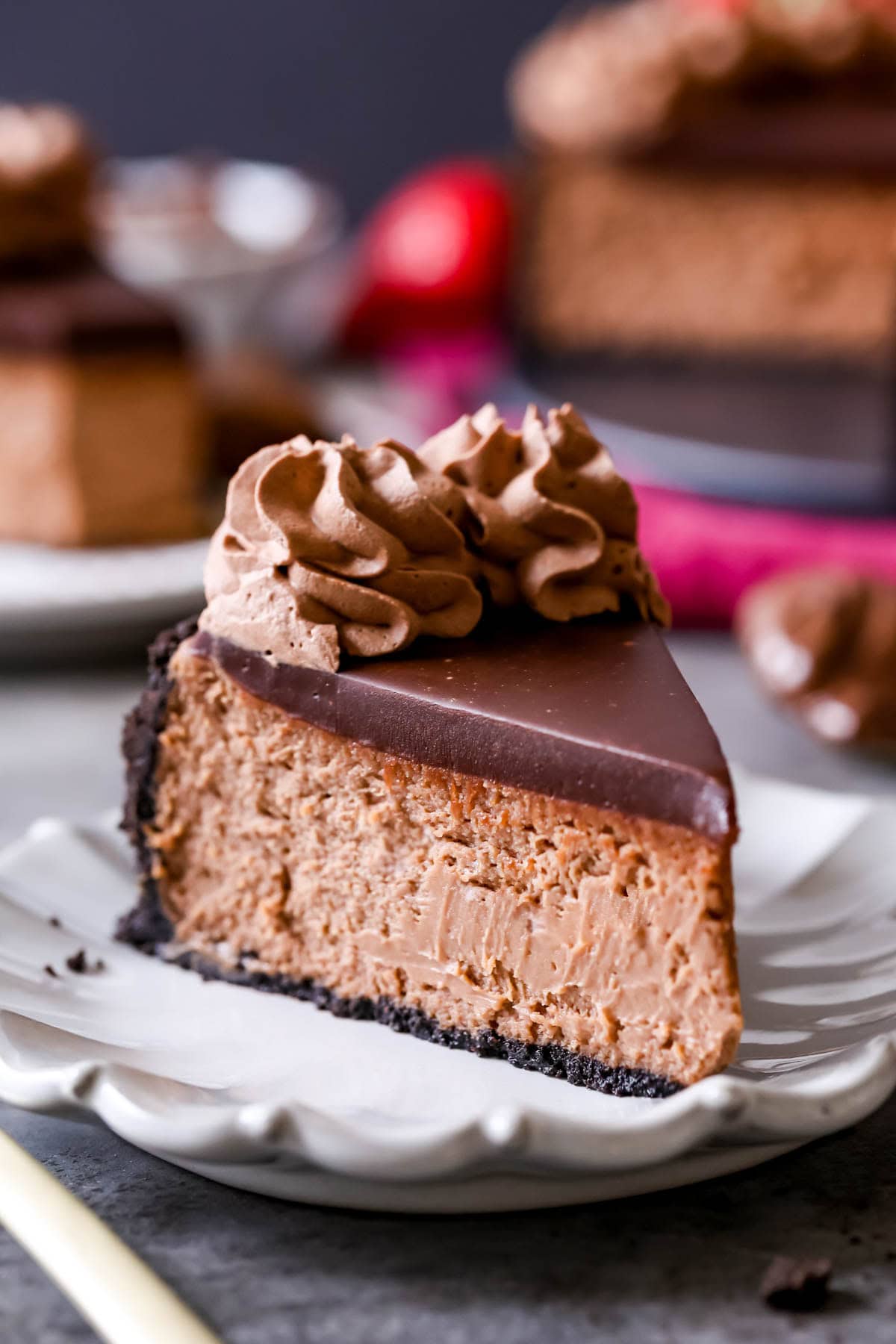 Slice of Nutella cheesecake topped with chocolate ganache and chocolate whipped cream. on a plate.