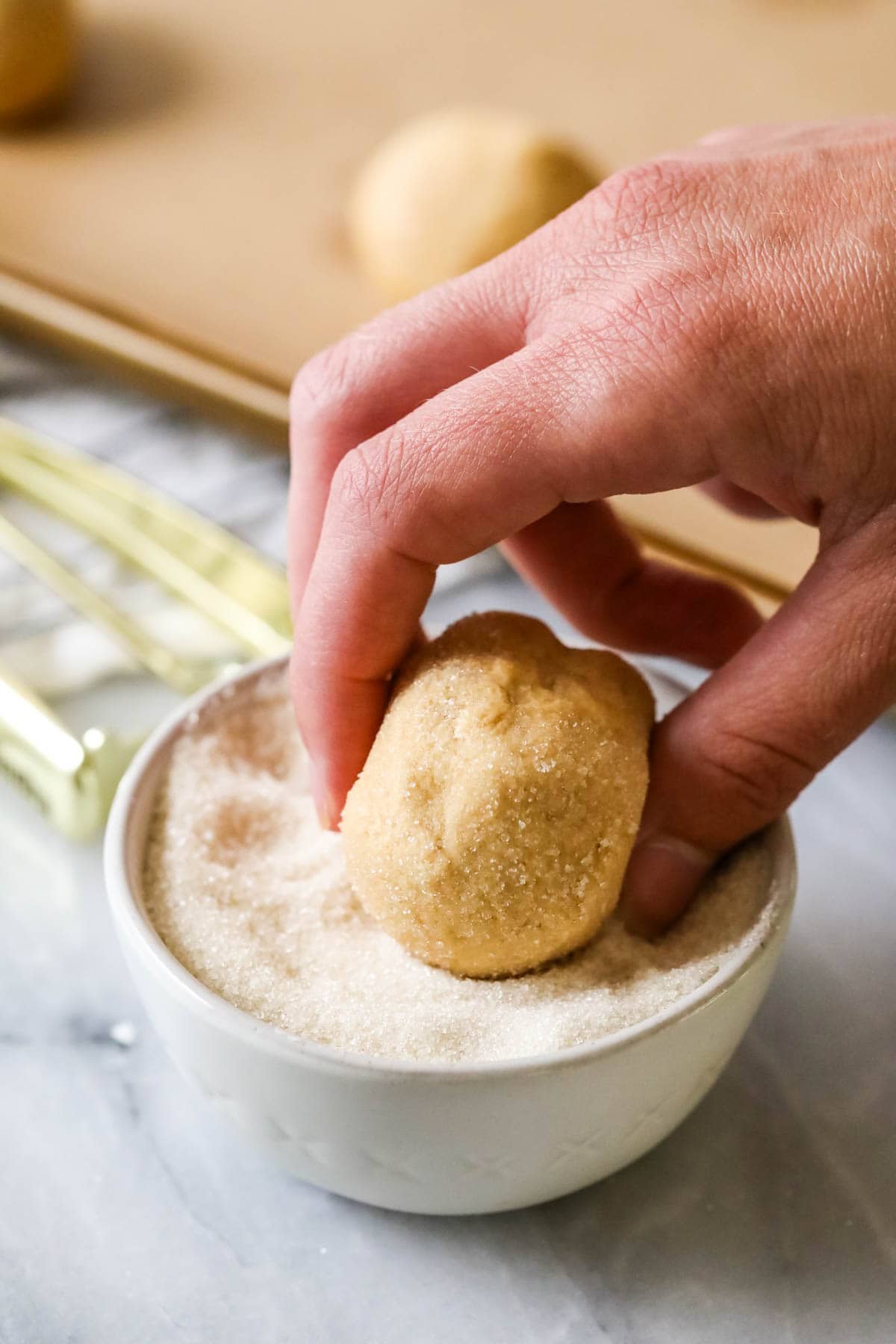 Rolling a cookie dough ball through granulated sugar.