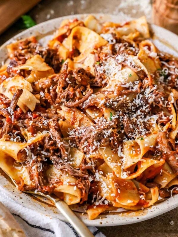 Plate of short rib ragu over pappardelle pasta topped with grated parmesan cheese.