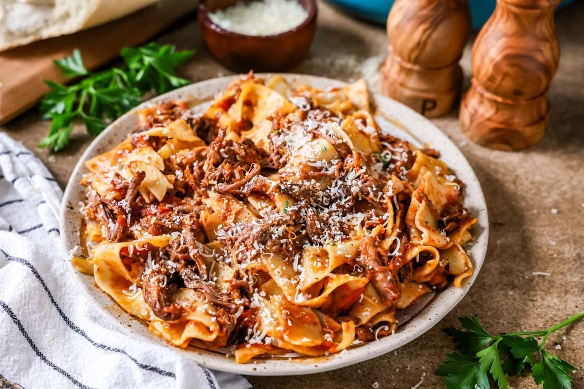 Plate of short rib ragu over pappardelle pasta topped with grated parmesan cheese.