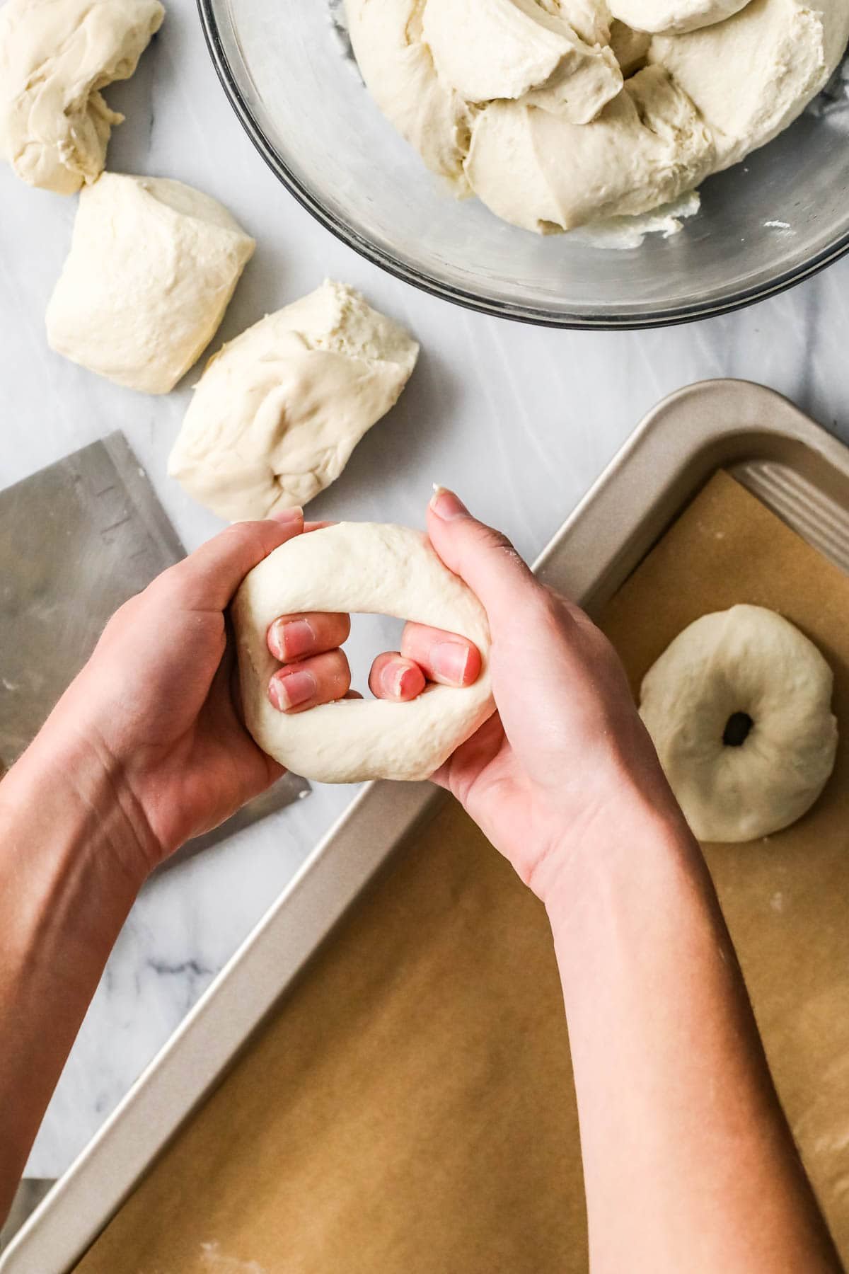 Hands stretching a hole into a dough ball to make a bagel.
