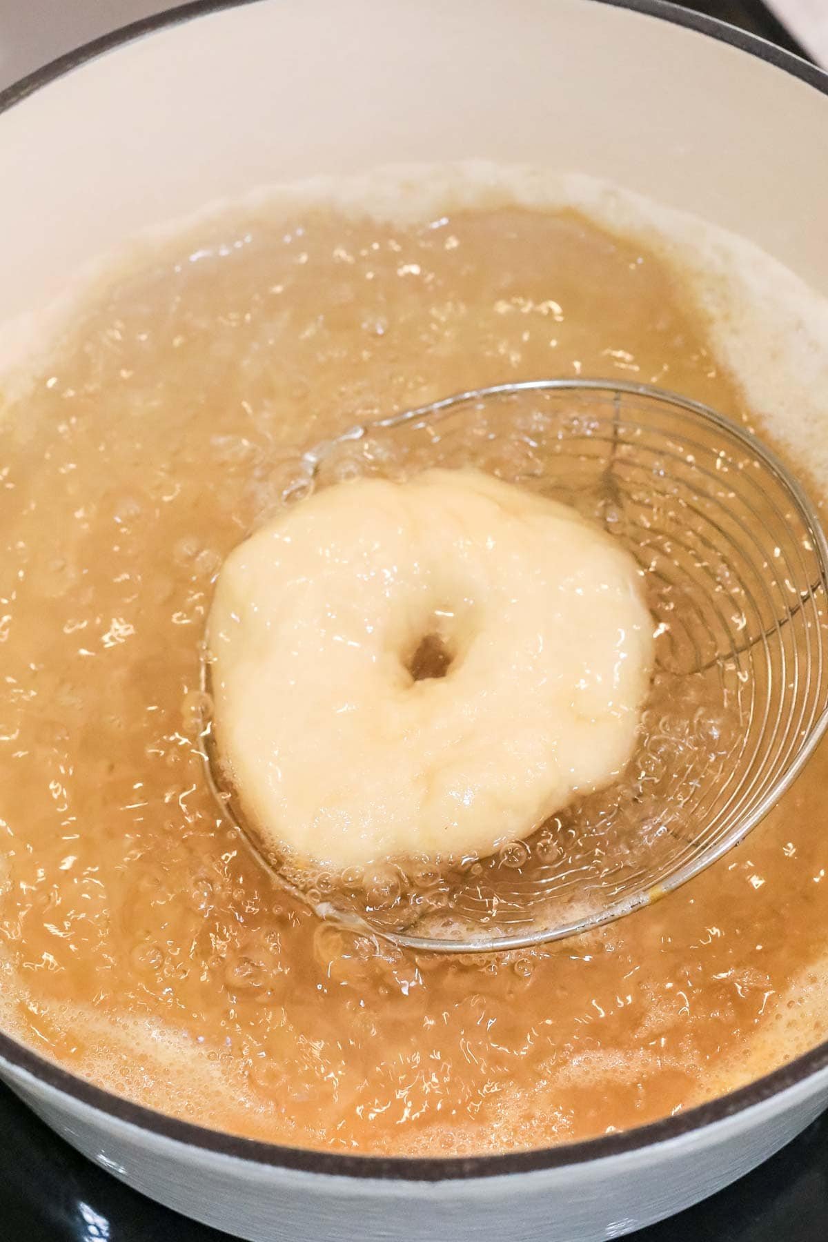 Bagel being dipped into a boiling water and honey mixture before baking.