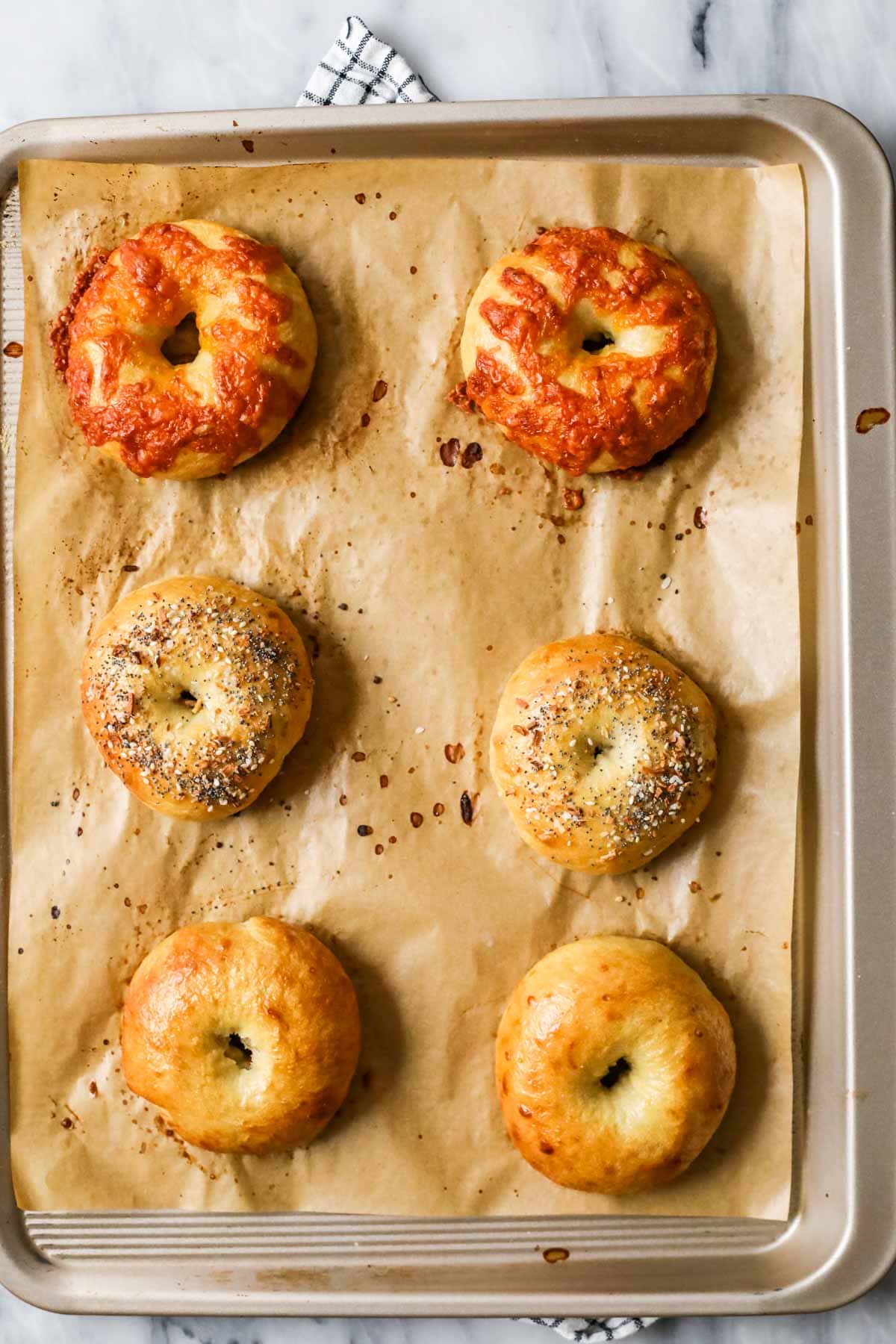 Overhead view of a tray of homemade sourdough bagels, with three different flavors on the tray.