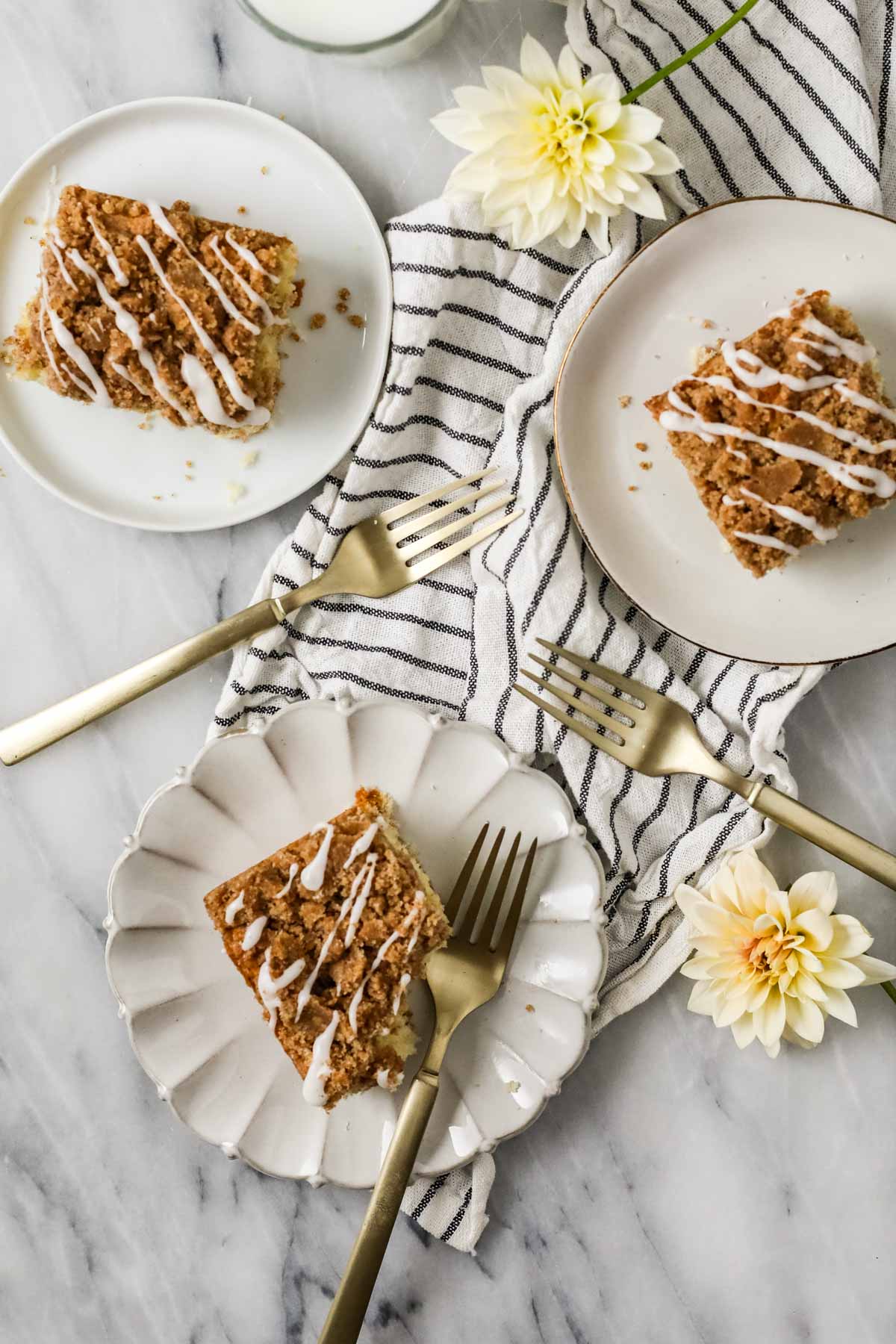 Overhead view of slices of coffee cake on white plates with a striped towel underneath.
