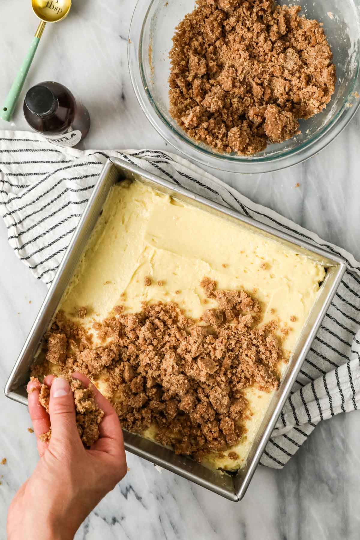Overhead view of streusel being sprinkled over a square pan of coffee cake batter.
