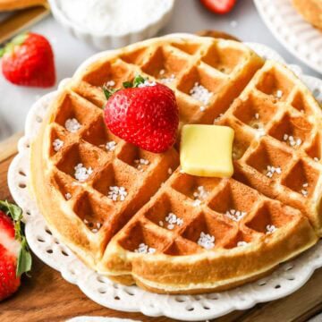 Sourdough waffle on a plate topped with a strawberry, a pat of butter, and Belgian pearl sugar.