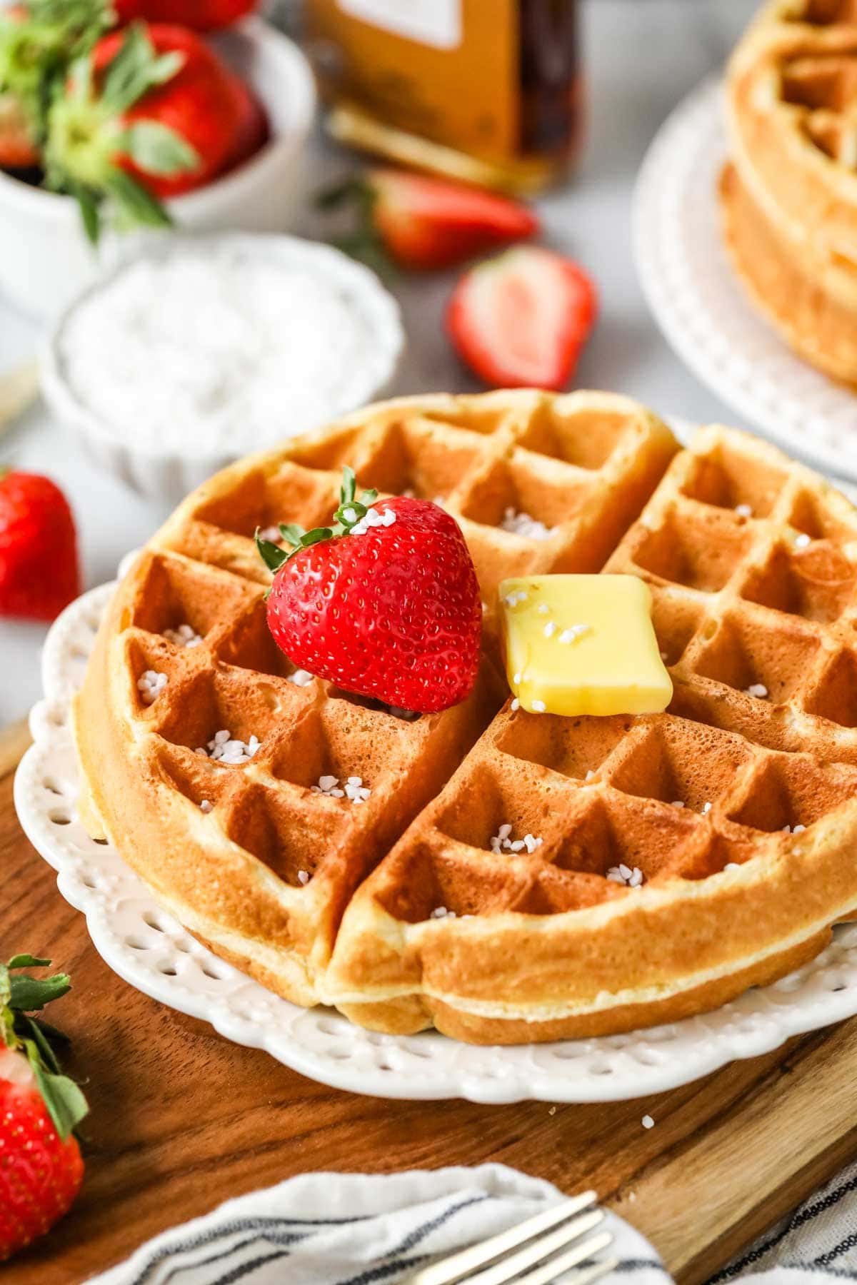 Sourdough waffle on a plate topped with a strawberry, a pat of butter, and Belgian pearl sugar.
