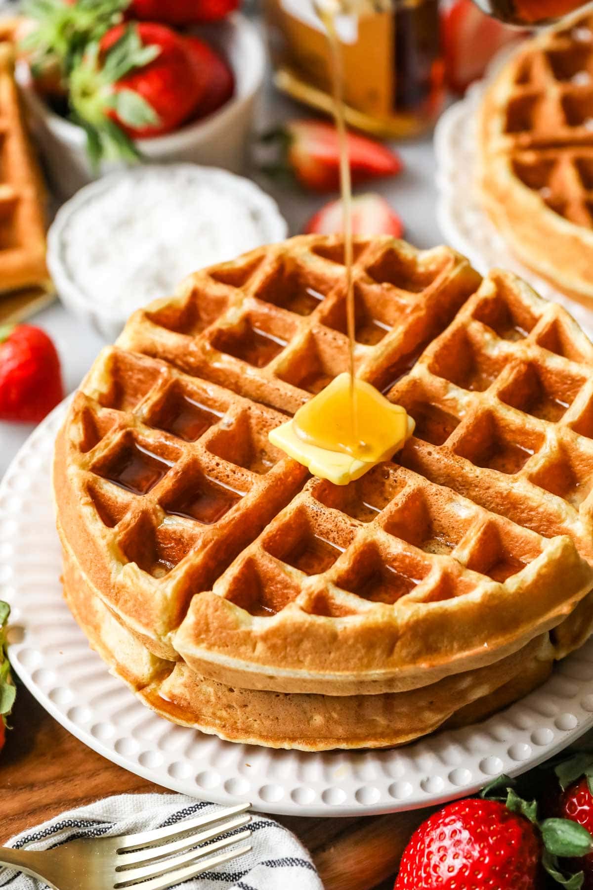 Maple syrup being poured over a stack of two belgian waffles made with sourdough discard.