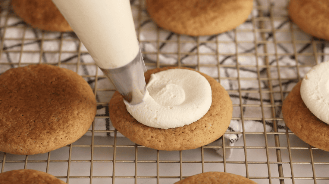Piping a swirl of mascarpone frosting onto tiramisu cookies.
