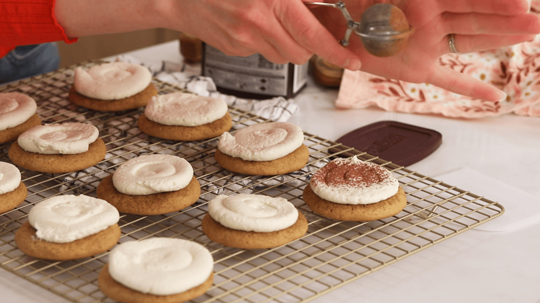 Dusting cocoa powder over frosted tiramisu cookies.