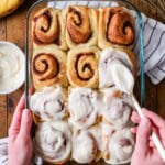 Overhead view of banana bread cinnamon rolls being frosted with cream cheese icing.